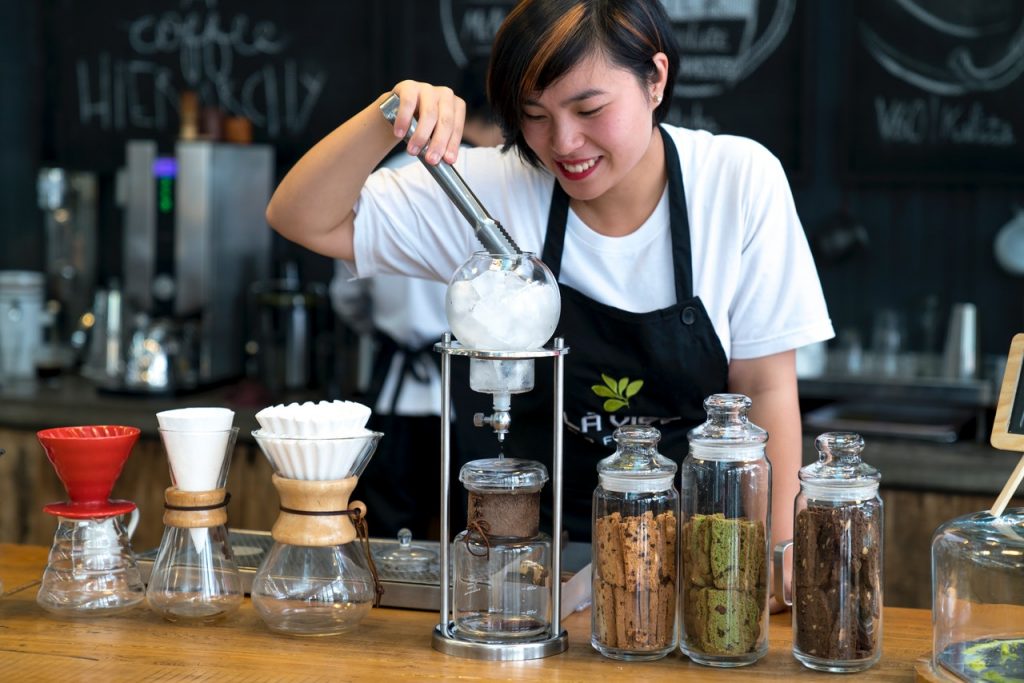 Young business owner at coffee shop wearing branded apron.